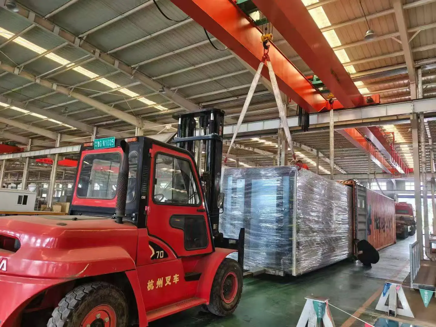 Wrapped expandable house being loaded by forklift inside workshop